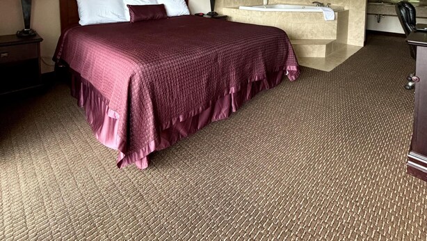 A hotel room with a large bed, two bedside lamps, a framed picture on the wall, a bathtub, and a desk with a chair.
