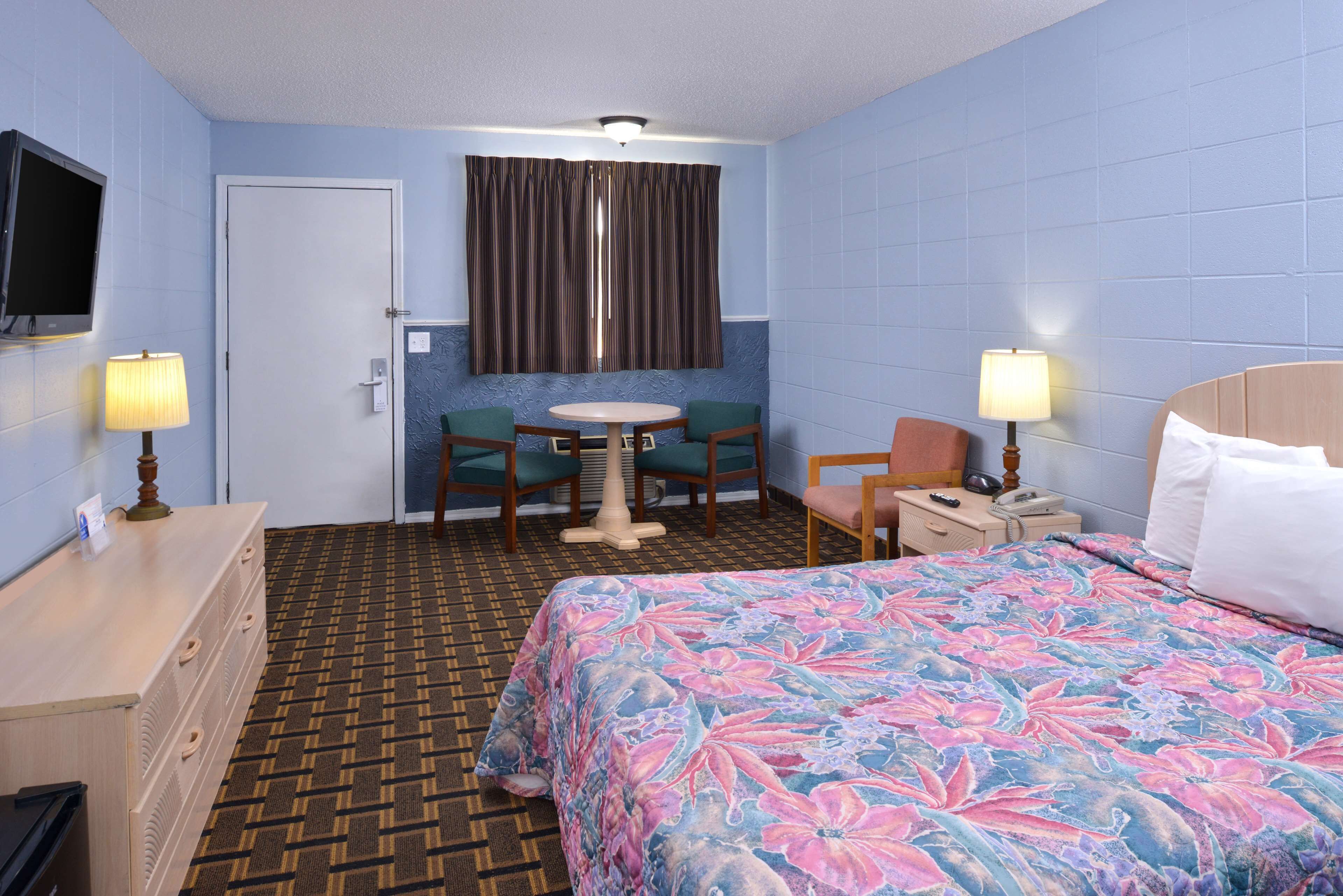 A hotel room with a bed, a desk, a chair, a TV, and a window with curtains.