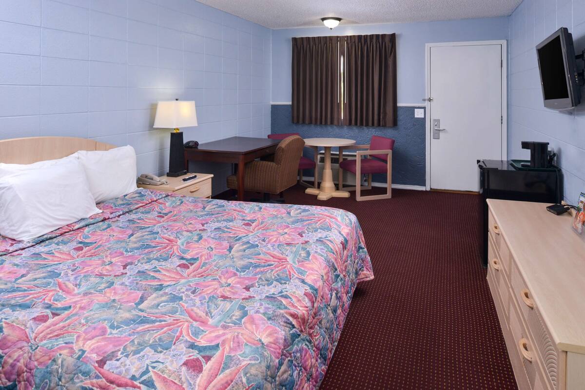 Una camera d'albergo con un letto, una scrivania, una sedia, un tavolo, una TV e un comò.