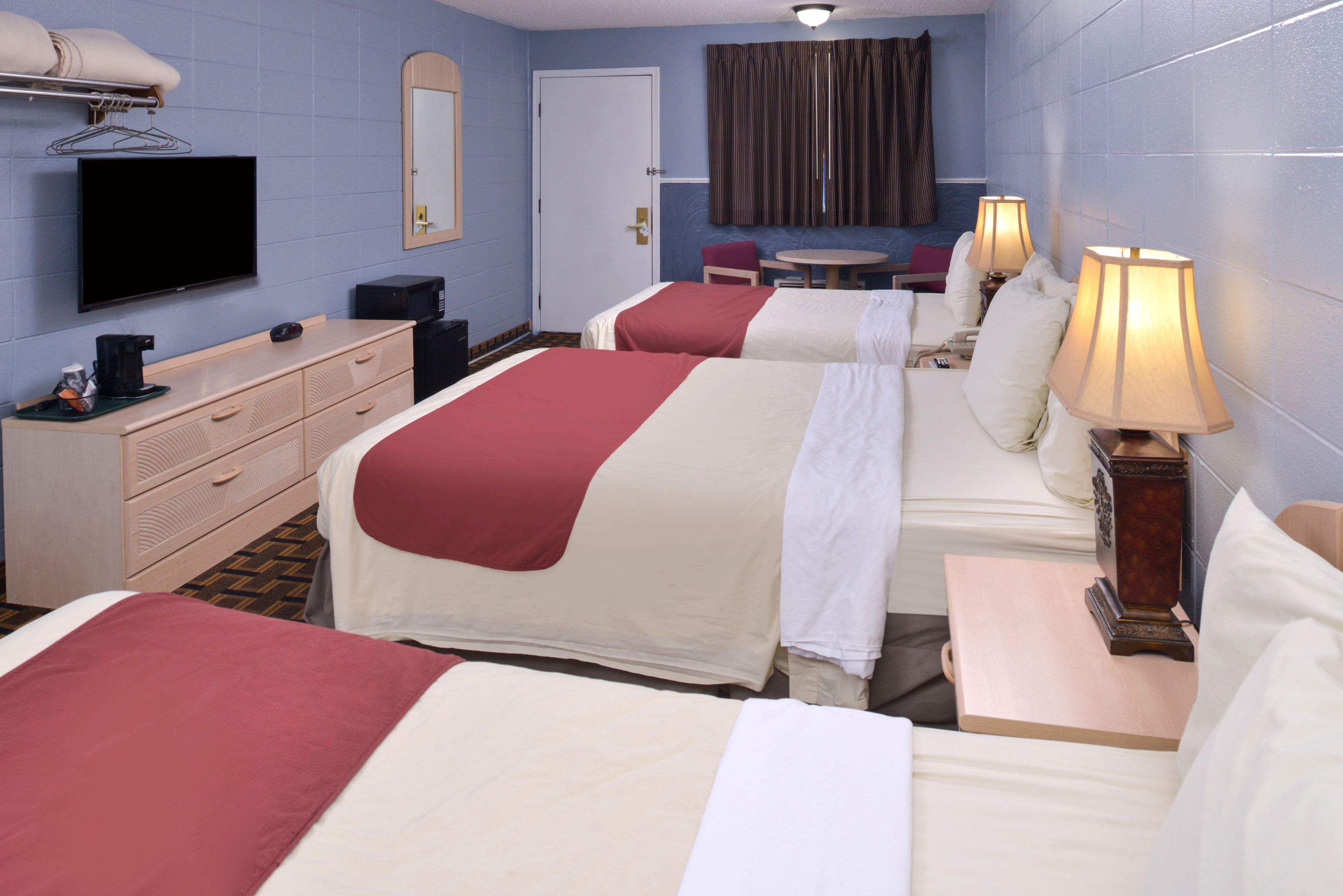 A hotel room with two beds, a television, a desk, and a small table with lamps.