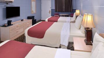 A hotel room with two beds, a television, a desk, and a small table with lamps.
