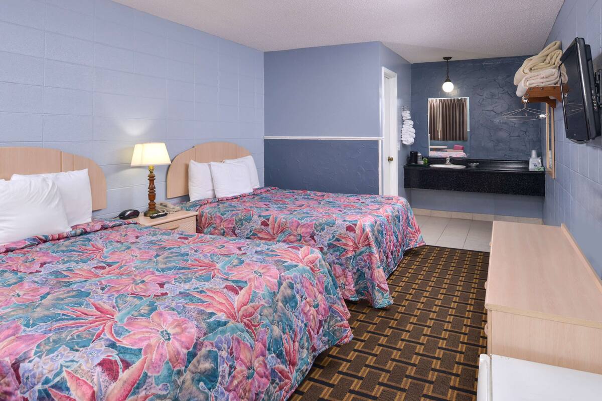 Una camera d'albergo con due letti, un bagno con uno specchio e un lavandino, e una TV fissata al muro.