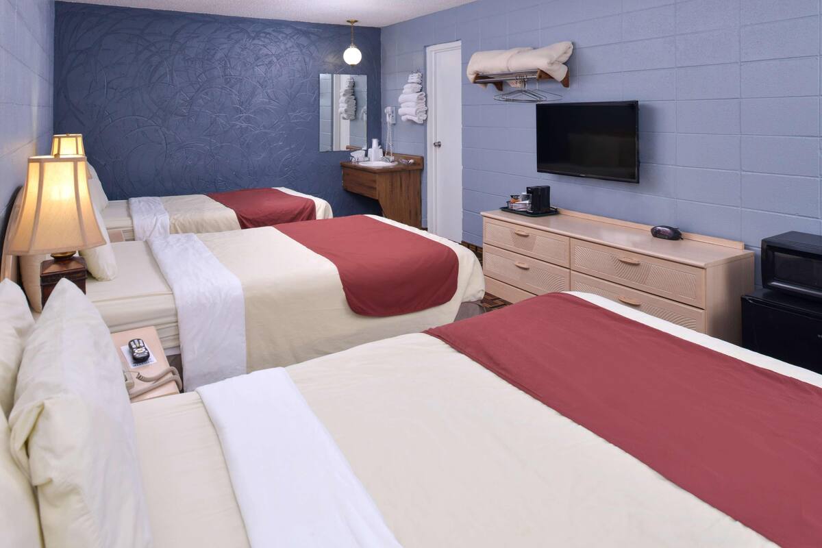 Una camera d'albergo con due letti, una televisione, una cassettiera, uno specchio e una lampada.