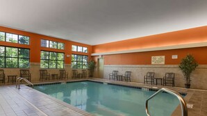 Una piscina interior con señalización clara, suelo de baldosas y zona de estar con sillas y mesas.