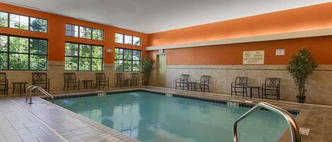 An indoor swimming pool with clear signage, a tiled floor, and a seating area with chairs and tables.