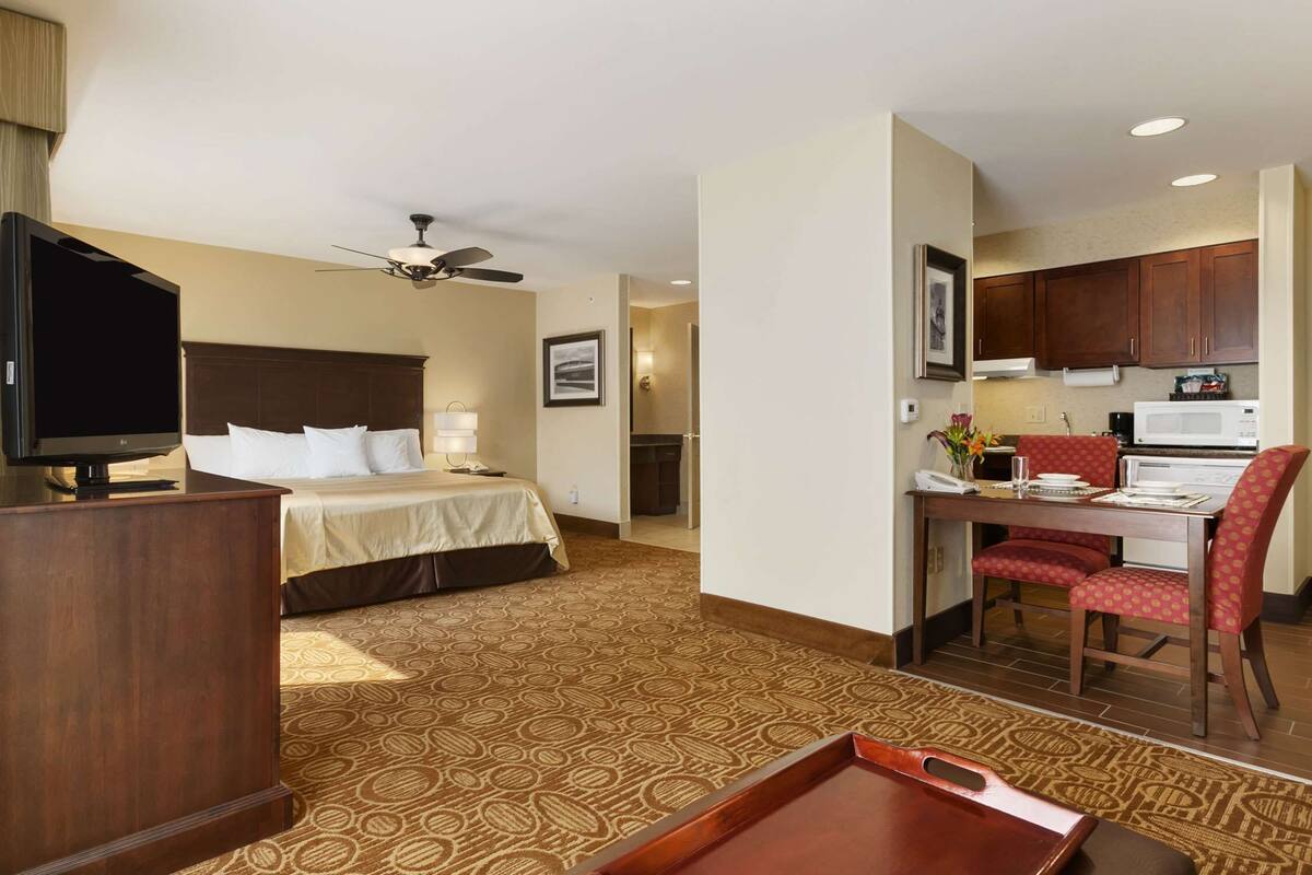 Habitación de hotel con cama, escritorio, televisión y kitchenette.