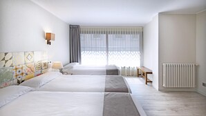 A hotel room with two beds, a bedside table, a lamp, a radiator, and a window with sheer curtains. - Hotel Tudel (Escaldes-Engordany)