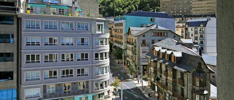 A multi-story building with a café on the ground floor, a pharmacy on the right, and a view of a mountainous landscape in the background.