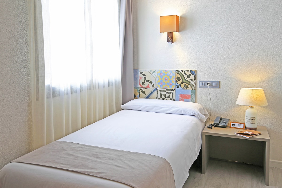 Une chambre d’hôtel comprenant un lit, une table de chevet avec une lampe, un téléphone et une tête de lit décorative.