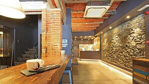 A bar area with a wooden counter, a coffee cup, and a stone wall. - Hotel Tudel (Escaldes-Engordany)