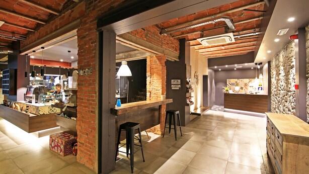 A modern interior with exposed brick walls, a bar area with stools, and a reception desk. - Hotel Tudel (Escaldes-Engordany)