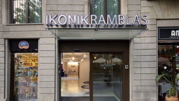 The exterior of a hotel named 'Ikonikramblas' with a modern glass entrance and a visible interior through the glass doors. - Ikonik Ramblas (Barcelona)