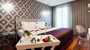 A hotel room with a bed, a bedside table with a bottle and glasses, a tray with flowers, and a patterned wall. - Ikonik Ramblas (Barcelona)