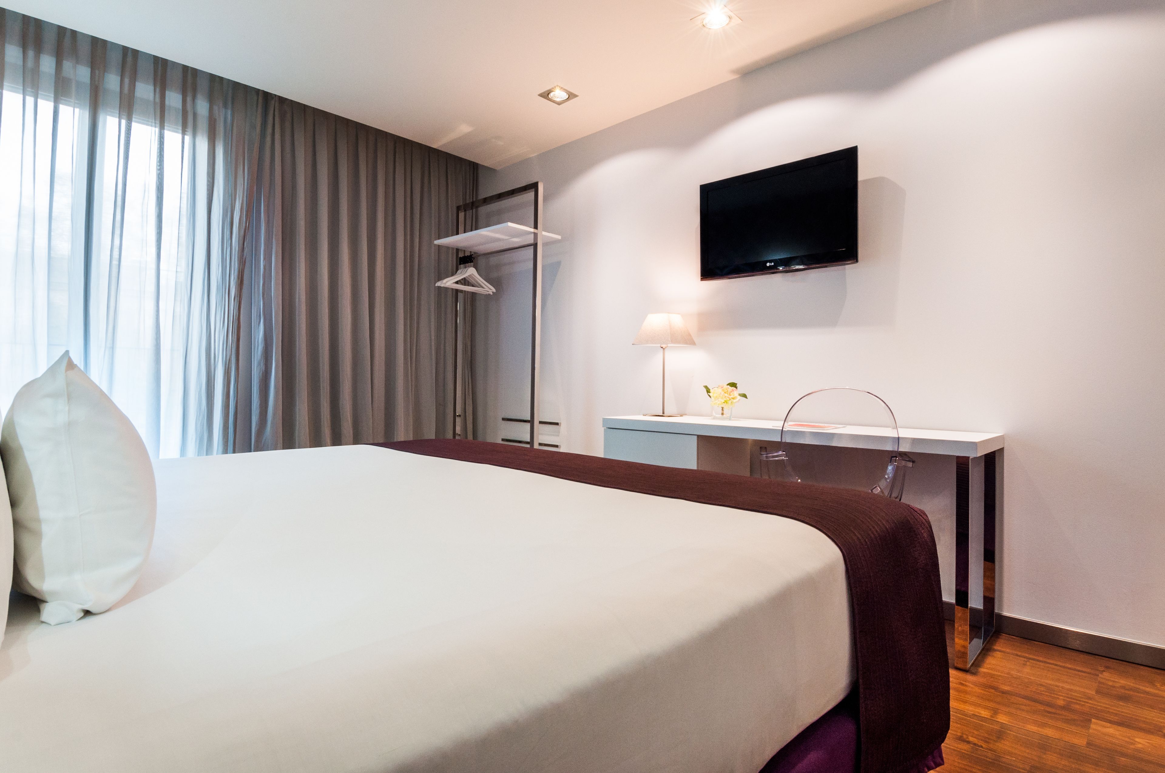 Habitación de hotel moderna con una cama grande, un escritorio, un televisor de pantalla plana y una ventana con cortinas.