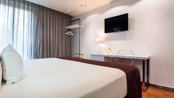 Habitación de hotel moderna con una cama grande, un escritorio, un televisor de pantalla plana y una ventana con cortinas.