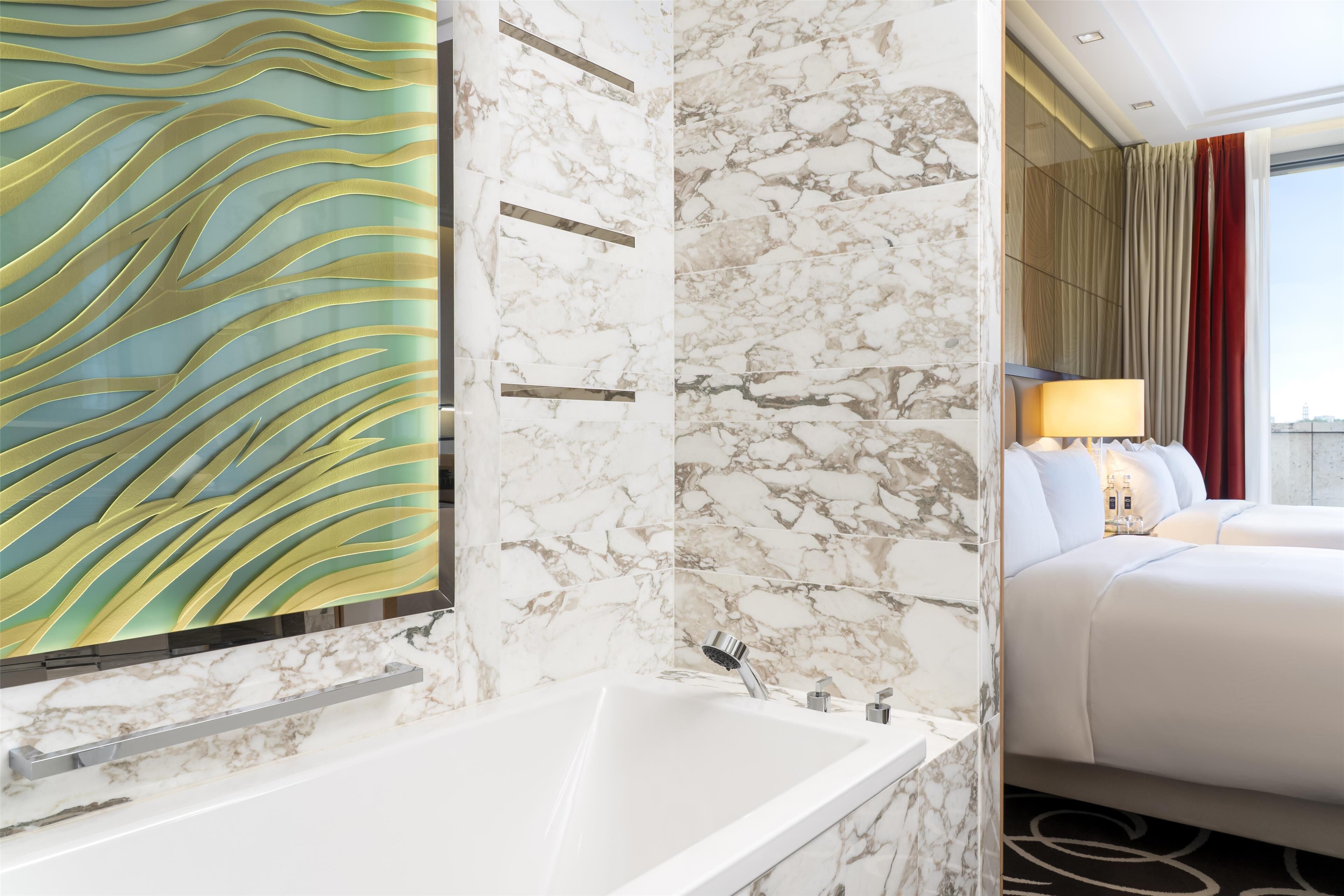 A modern hotel room with a marble bathroom, a large artwork on the wall, and a bed with a view of the city.