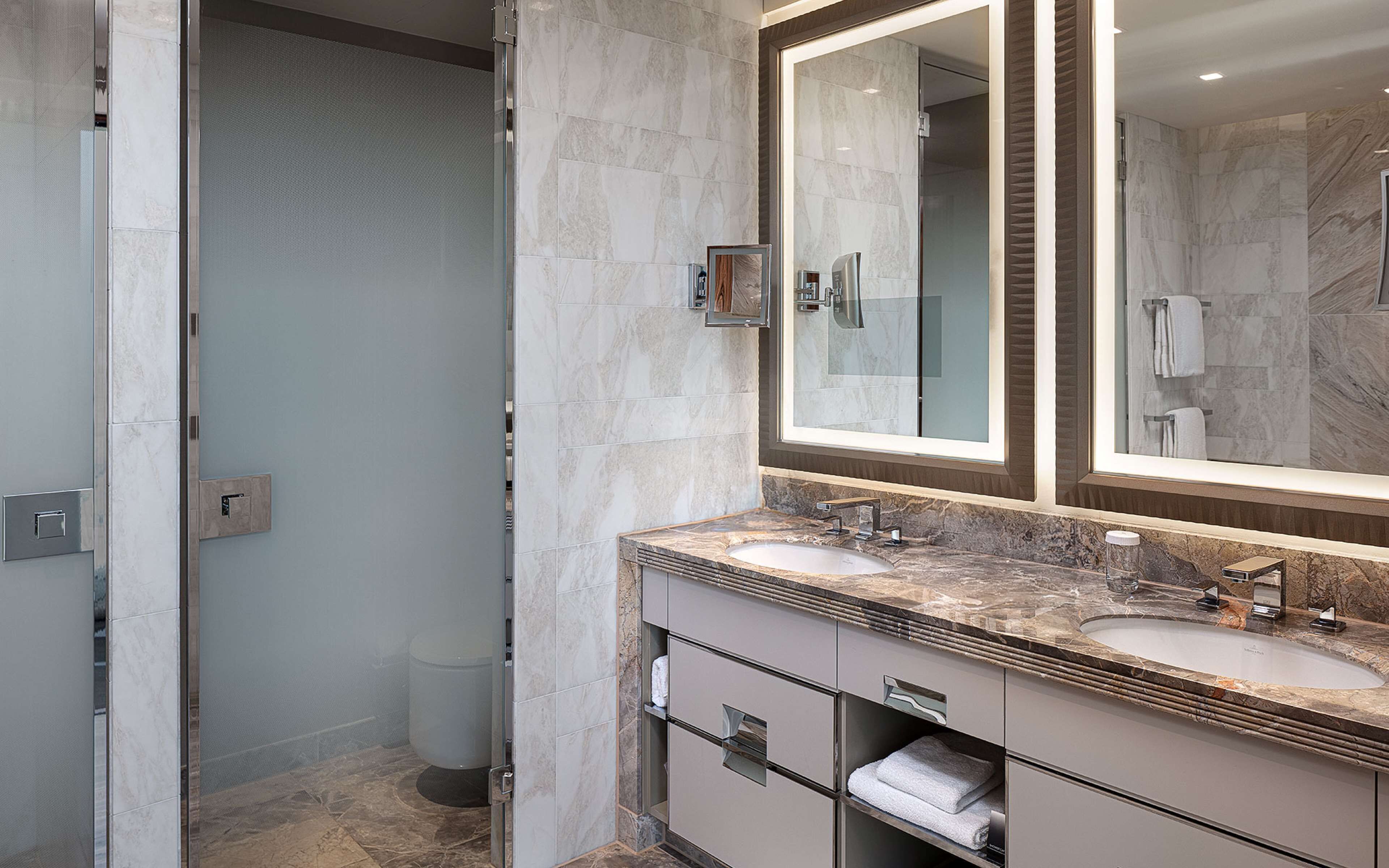 A modern bathroom with two sinks, a large mirror, and a shower area.