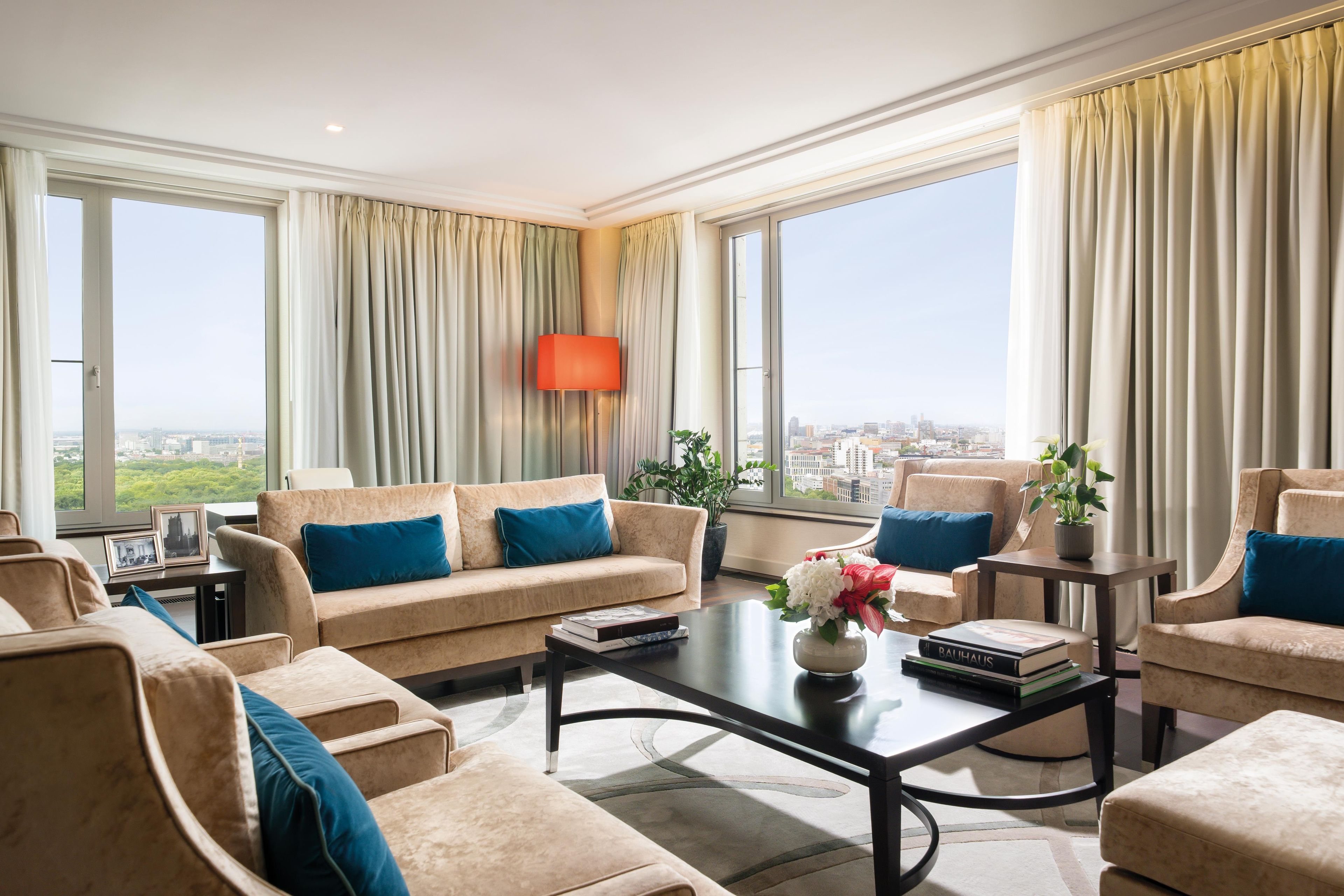 Uma sala de estar ampla com sofá, mesa de centro e vista para a cidade através de grandes janelas.