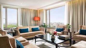 Uma sala de estar ampla com sofá, mesa de centro e vista para a cidade através de grandes janelas.