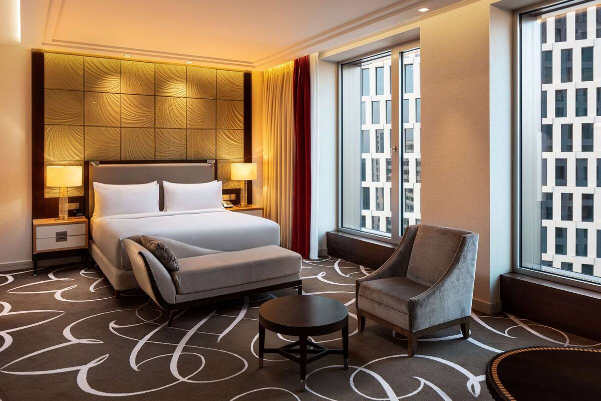 Habitación de hotel con cama, una silla, una mesita y ventana con vistas a edificios.