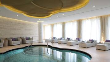 Un área de piscina interior moderna con sillones de descanso y un diseño de techo singular.