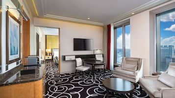 Habitación de hotel con un ventanal grande, un televisor de pantalla plana, una mesa redonda de comedor, dos sillones y un sofá.