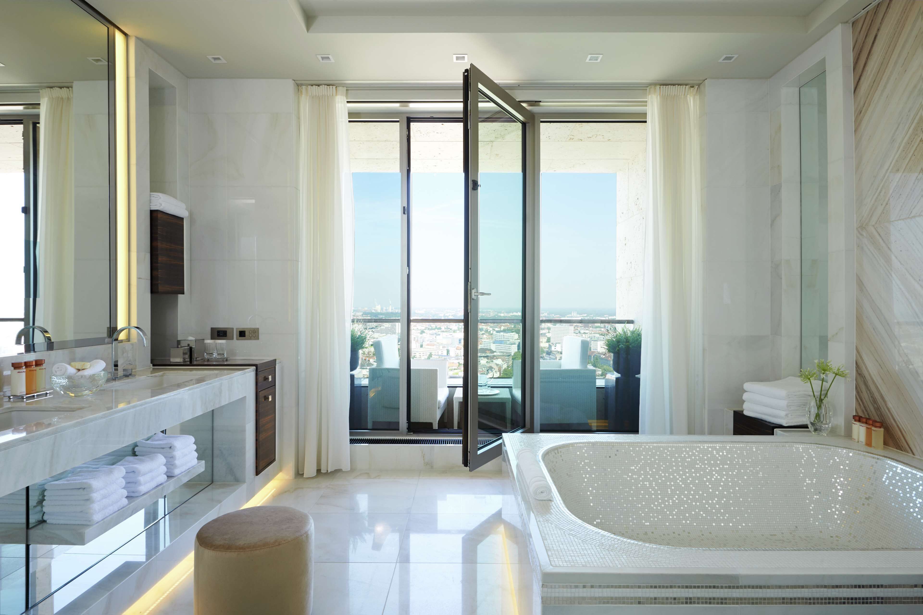 A modern bathroom with a large bathtub, a vanity with a mirror, and a view of the city through a glass door.