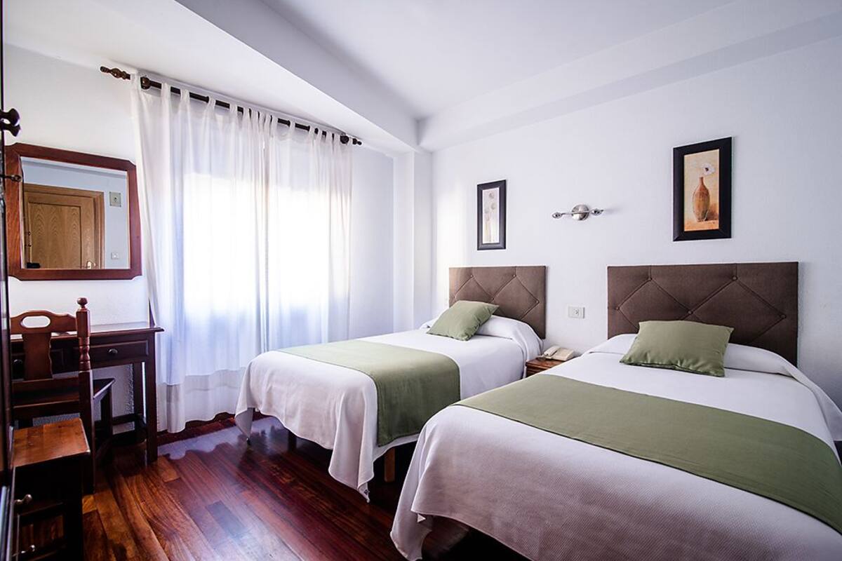 A hotel room with two beds, a desk, a chair, and a window with curtains.