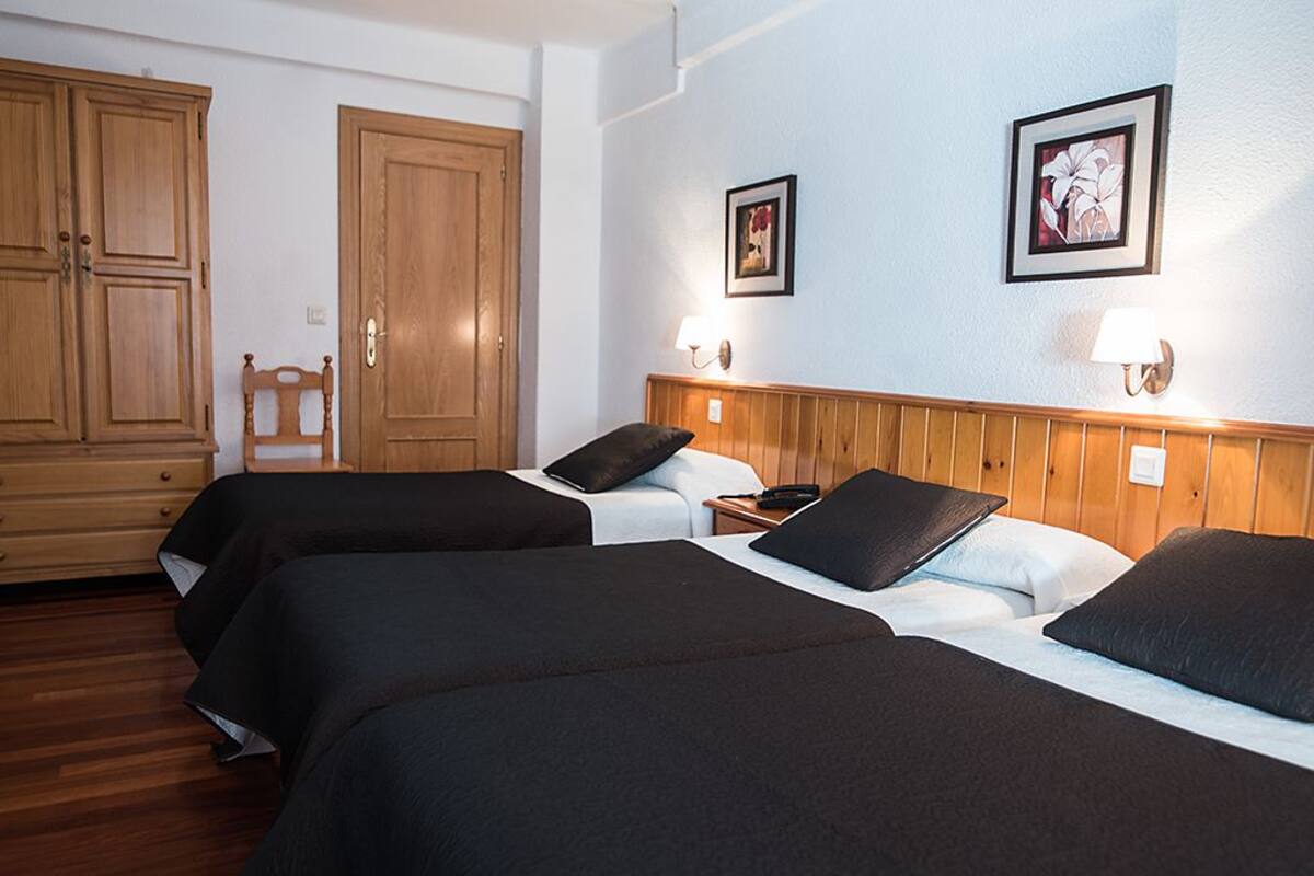 A hotel room with two beds, wooden wardrobe, and two wall-mounted lamps.