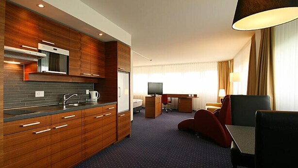 Een moderne hotelkamer met een kitchenette, een flatscreen televisie, een bureau en een comfortabele zithoek.