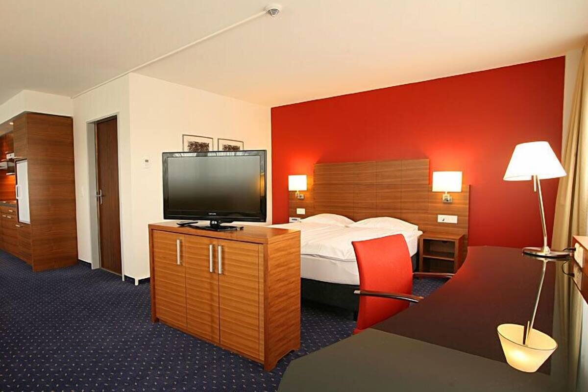 A hotel room with a bed, a TV on a wooden cabinet, a desk, and a lamp.