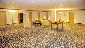Een ruime kamer met een kamerbreed tapijt, een zithoek met een tafel, en een deur op de achtergrond.