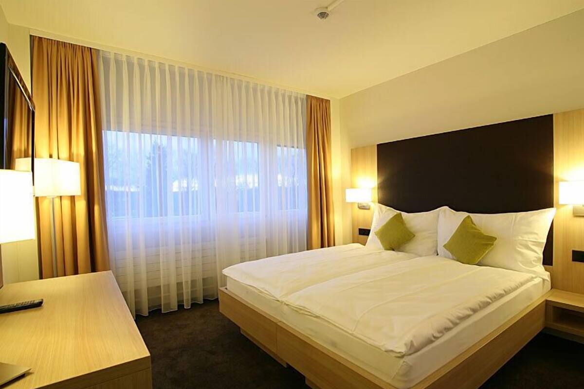 A hotel room with a large bed, two bedside lamps, a desk, and a window with curtains.