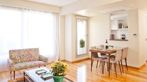 A living room with a floral sofa, a dining table with chairs, a coffee table, and a potted plant.