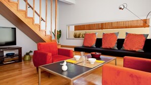 A modern living room with a staircase, red sofas, a coffee table, and a television.