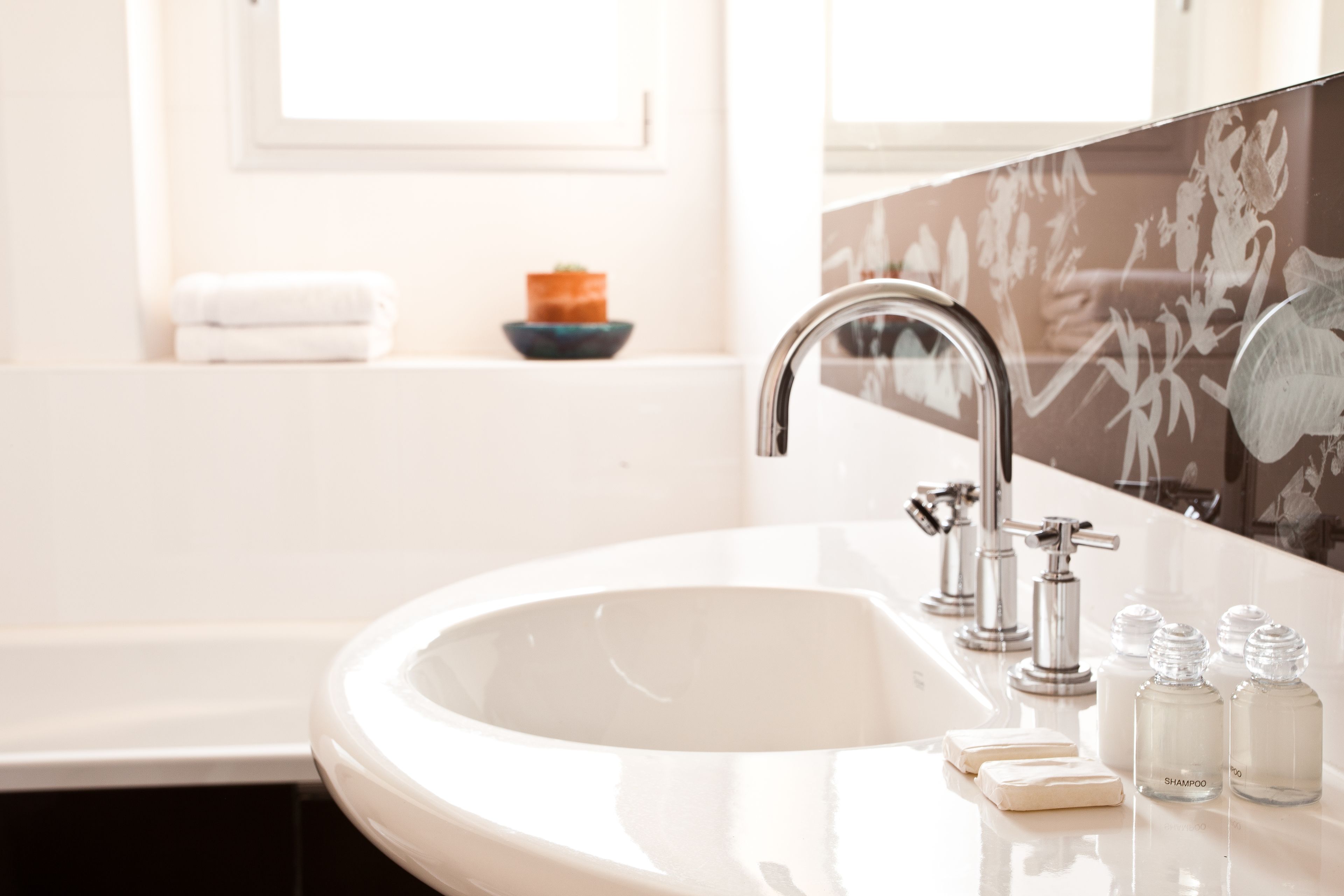 A bathroom with a white sink, a mirror, and a bathtub. There are toiletries on the sink and a towel on the wall.