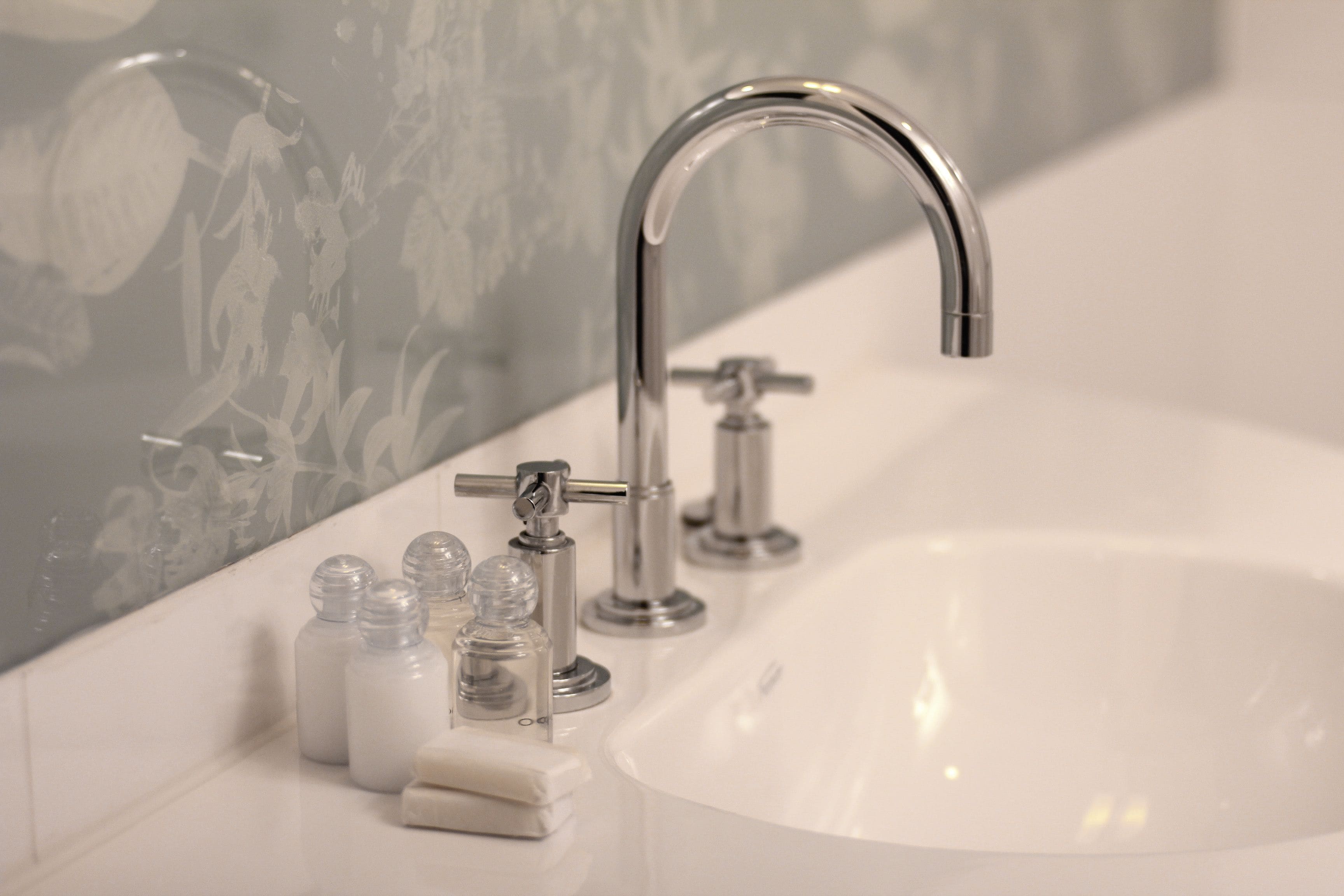 A bathroom with a white sink, a chrome faucet, and clear glass bottles likely containing toiletries.