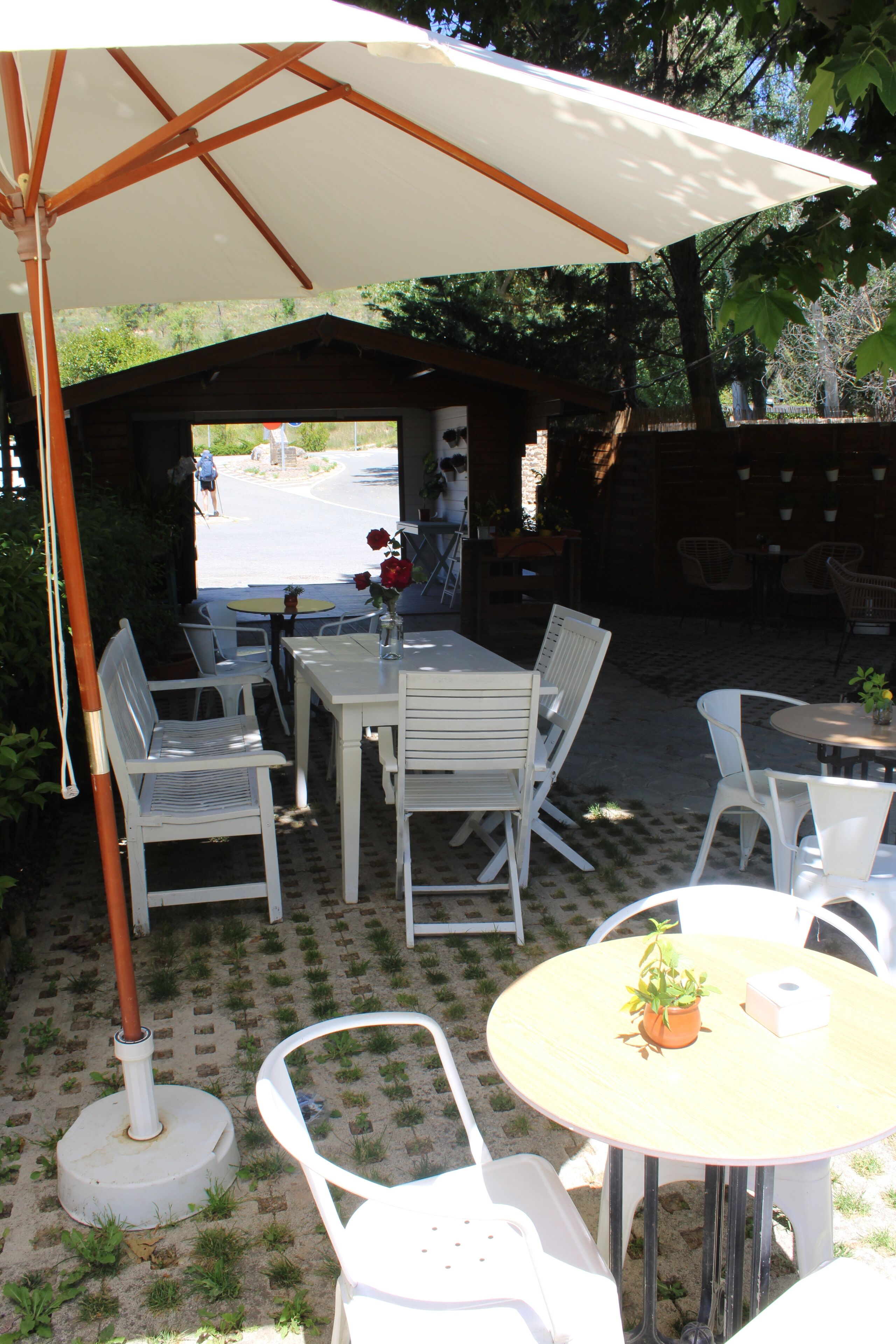 An outdoor patio with white chairs and tables, a covered area with a table and chairs, and a view of the street in the background.
