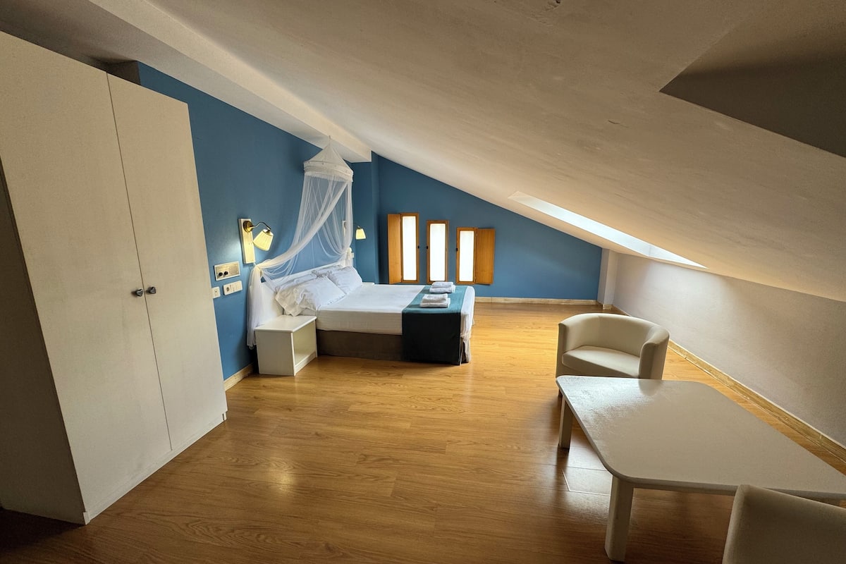 Un dormitorio con cama, mesita de noche, silla, armario y ventana con cortinas.