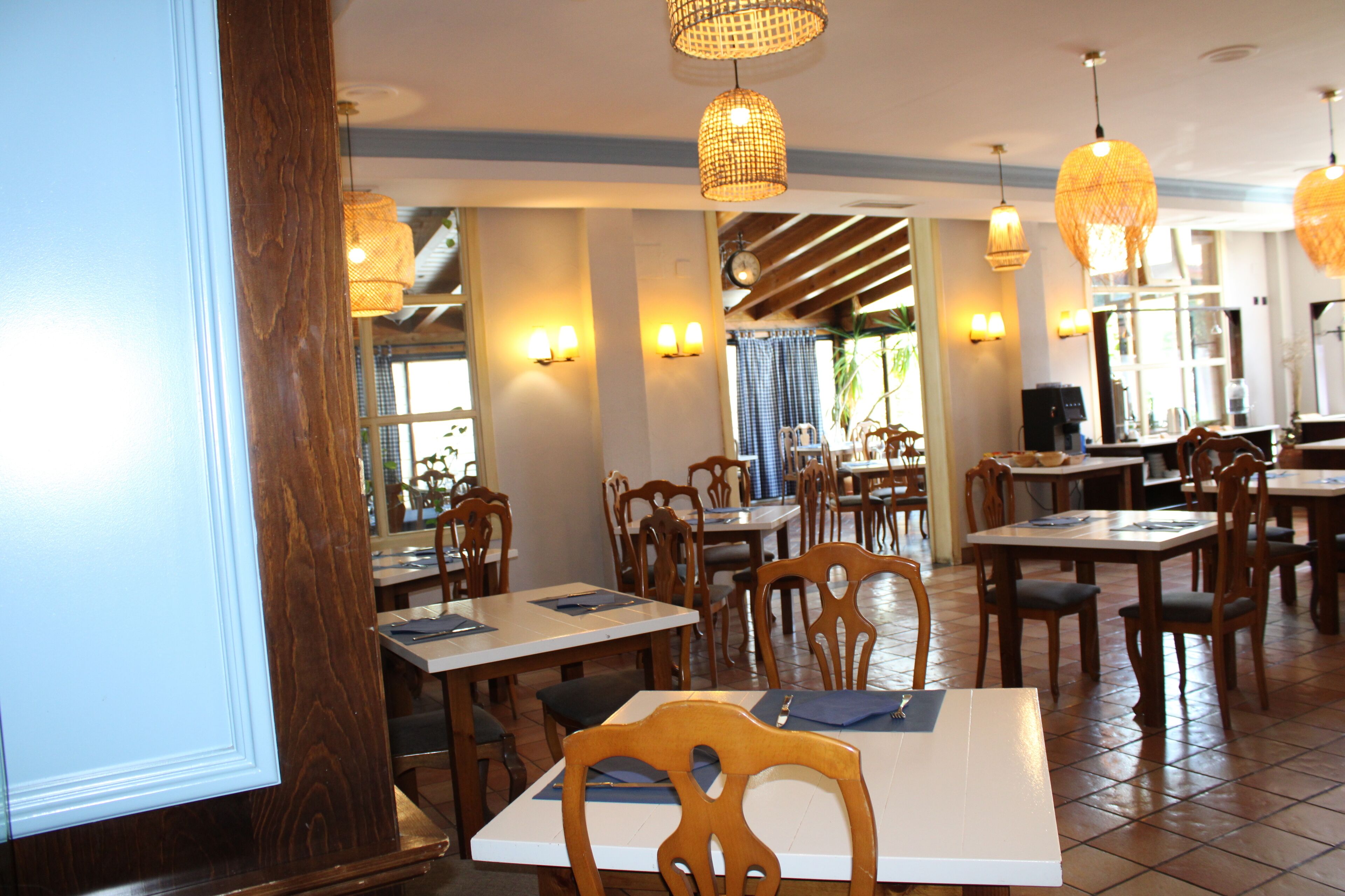 Een restaurantinterieur met houten tafels en stoelen, hanglampen en een betegelde vloer.