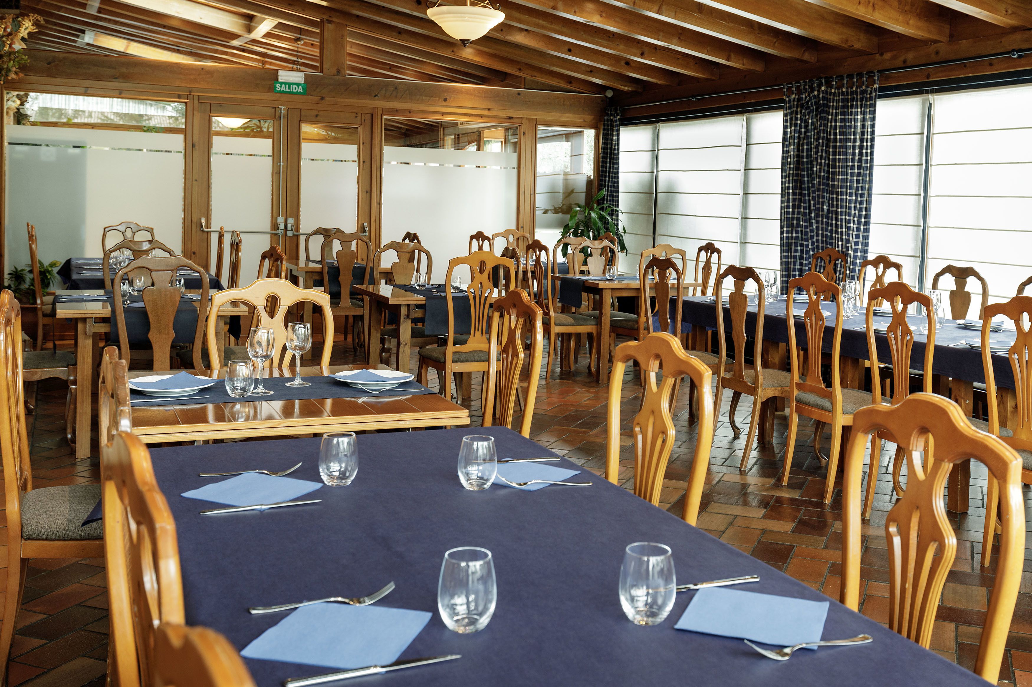 En restaurant med træborde og -stole, blå dug og et skilt der viser udgangen.
