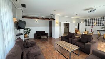 A spacious living area with multiple sofas and a coffee table, a television mounted on the wall, and a ceiling-mounted projector.