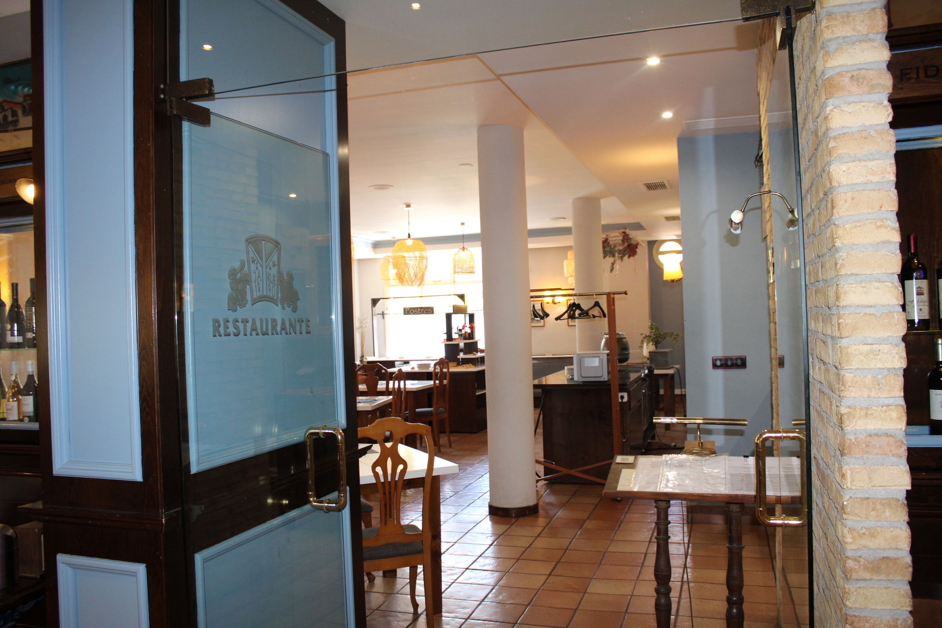A restaurant interior with a glass door, wooden chairs, a tiled floor, and a hanging light fixture.