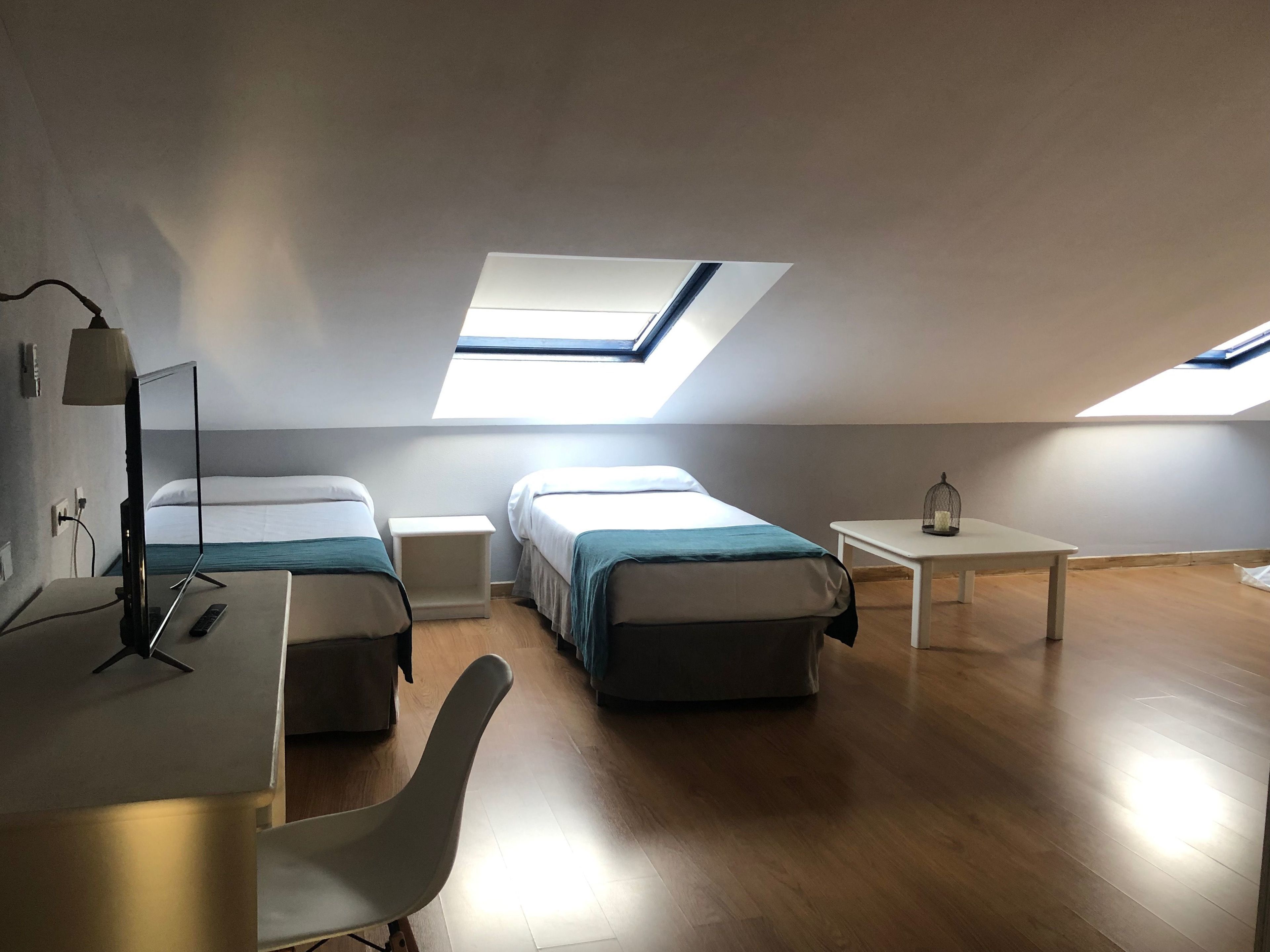 Una habitación moderna y bien iluminada con dos camas, un escritorio y un tragaluz.