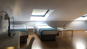 Una habitación moderna y bien iluminada con dos camas, un escritorio y un tragaluz.