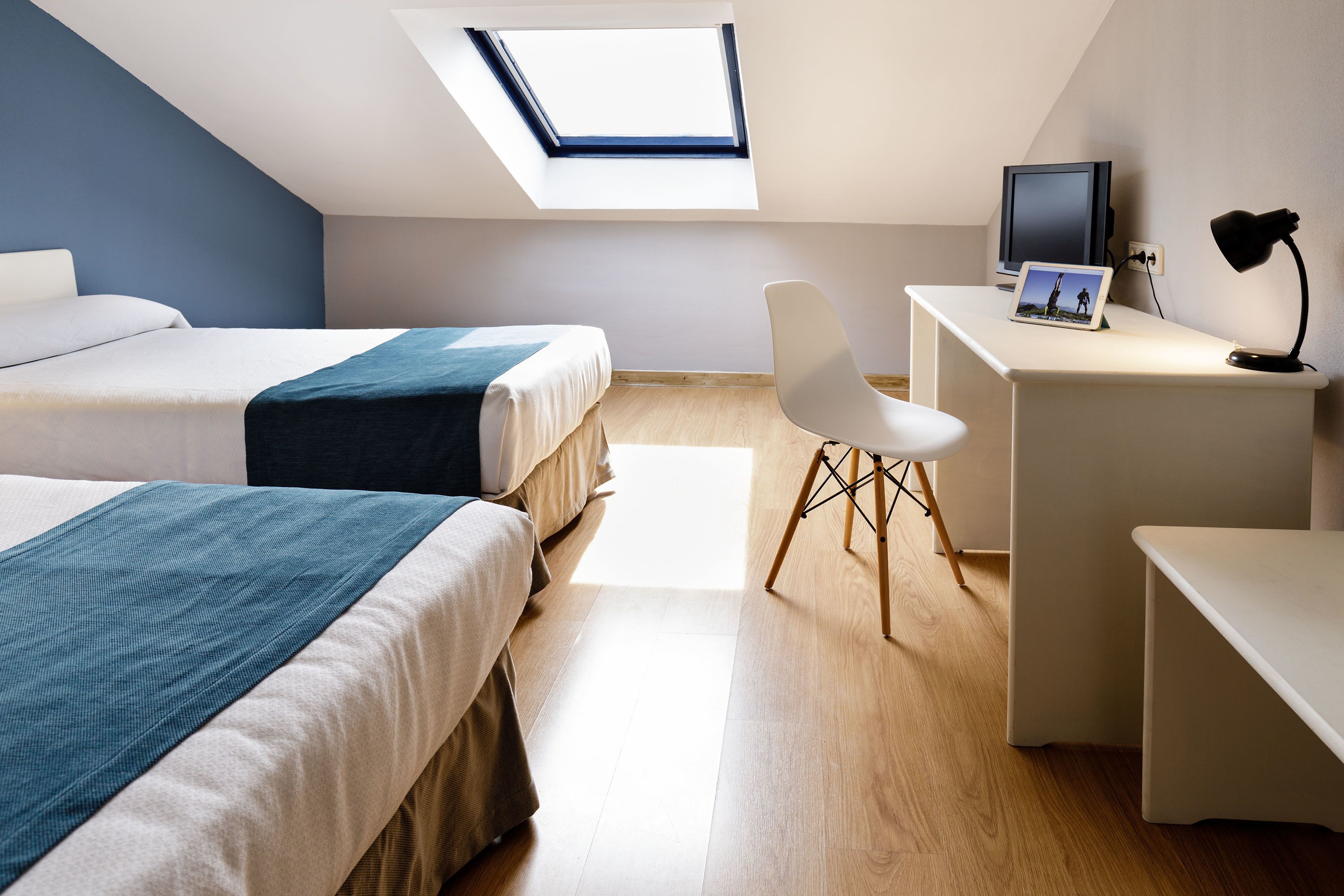 Quarto moderno com duas camas, uma escrivaninha e um claraboia.