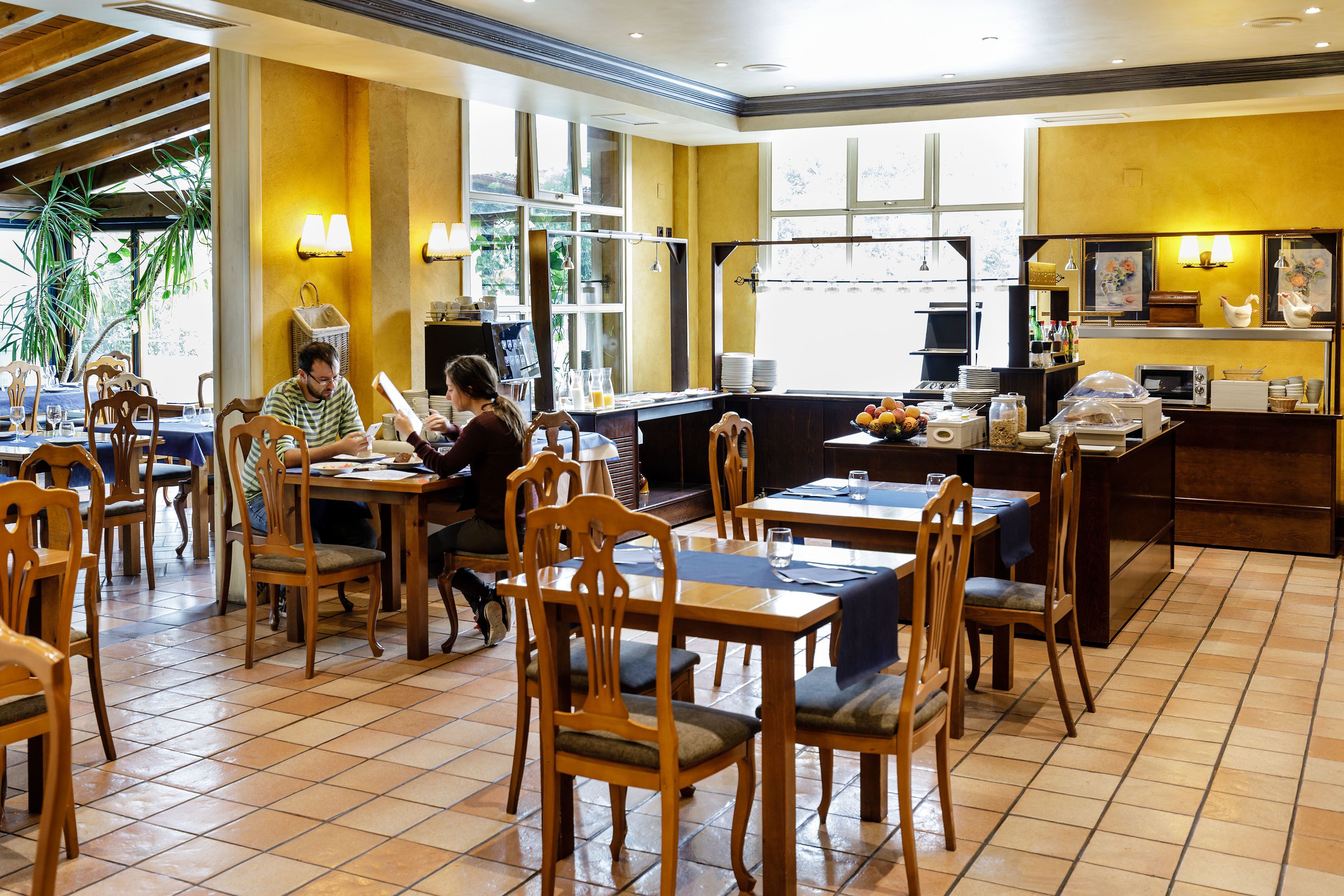 Un ristorante con tavoli e sedie in legno, un bancone con una cassa e un'ampia vetrata vista all'esterno.