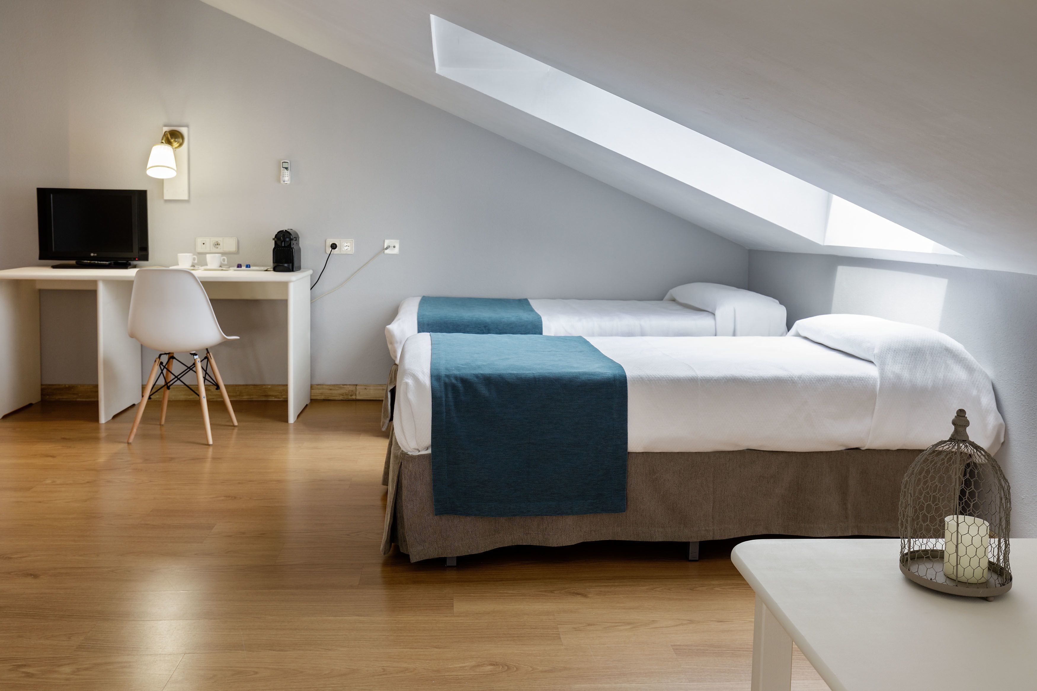 Un dormitorio moderno y minimalista con techo inclinado, un escritorio con computadora y una cama con manta azul.
