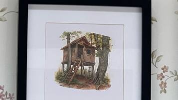 Een lijst met een foto van een houten boomhuis met een ladder, omringd door bomen en begroeiing.