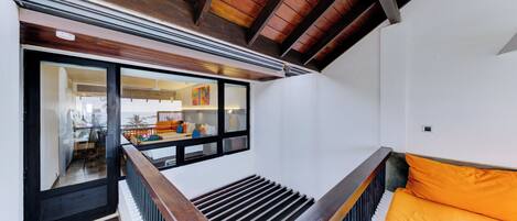 A staircase with wooden railings leading to a room with a sofa and a window overlooking a dining area.
